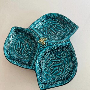 Puede incluir: Una fuente de cer&aacute;mica turquesa con tres secciones, con intrincados patrones florales y de remolinos. La fuente tiene un asa dorada en el centro. El dise&ntilde;o est&aacute; en relieve, creando una superficie texturizada. La fuente se utiliza probablemente para servir aperitivos.
