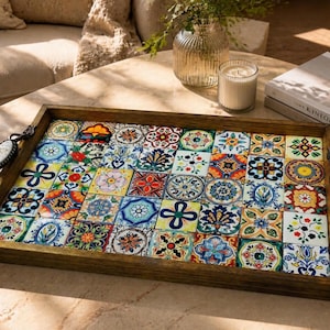 Puede incluir: Una bandeja de servicio rectangular de madera con un mosaico de azulejos de cerámica coloridos y estampados. La bandeja tiene bordes de madera marrón oscuro y dos asas de metal ornamentadas a los lados, con una incrustación de cerámica blanca.