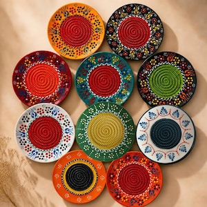 May include: A collection of ten circular ceramic grater plates arranged in a cluster. Each plate features a central textured spiral surface for grating surrounded by a decorative border with colorful floral and flame-like patterns in various hues.