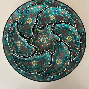 May include: A teal ceramic serving dish with a floral design. The dish is divided into six sections, each with a curved shape. The floral pattern includes white, red, and orange flowers. The rim is black with white dots.