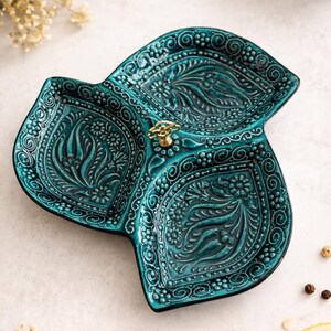 Puede incluir: Bandeja de cer&aacute;mica turquesa con tres secciones y un dise&ntilde;o floral en relieve. La bandeja tiene un asa dorada. El dise&ntilde;o incluye espirales, puntos y motivos de hojas. Ideal para servir aperitivos, mide aproximadamente 25 cm de di&aacute;metro.