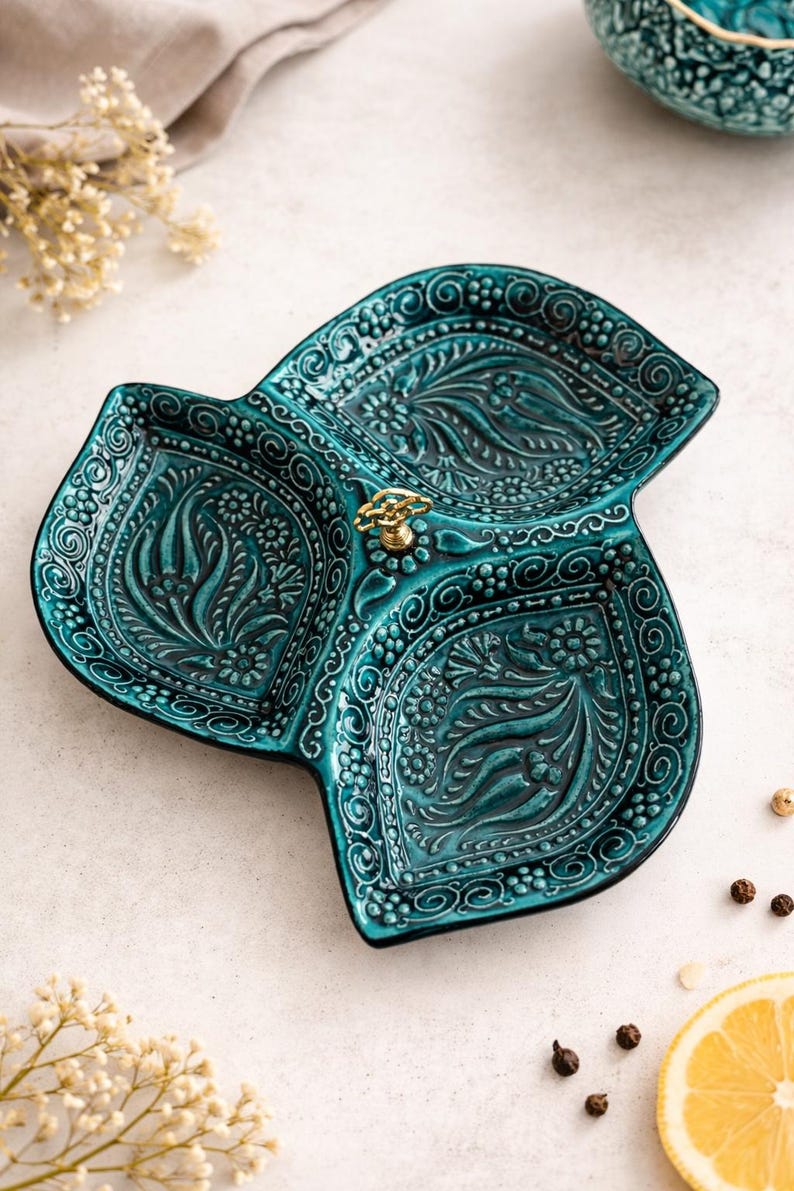 Puede incluir: Bandeja de cer&aacute;mica turquesa con tres secciones y un dise&ntilde;o floral en relieve. La bandeja tiene un asa dorada. El dise&ntilde;o incluye espirales, puntos y motivos de hojas. Ideal para servir aperitivos, mide aproximadamente 25 cm de di&aacute;metro.