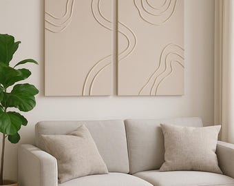 Op de afbeelding: Twee beige abstracte wandkunstpanelen met verhoogde, gebogen lijnen. De panelen zijn gemonteerd boven een lichtgrijze bank met bijpassende kussens. Een ronde, licht houten salontafel heeft een beige mok en een houten kom.
