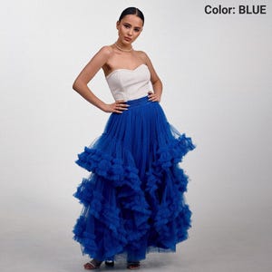 May include: A strapless white top paired with a vibrant blue tulle skirt. The skirt features multiple layers of ruffled fabric, creating a voluminous and textured appearance. The image is set against a plain white background.