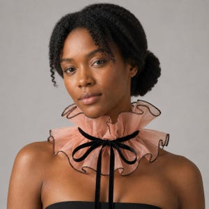 May include: A peach-colored ruffled collar with a black velvet bow and trim. The collar is made of a sheer fabric and is worn around the neck. The collar adds a touch of elegance and sophistication.