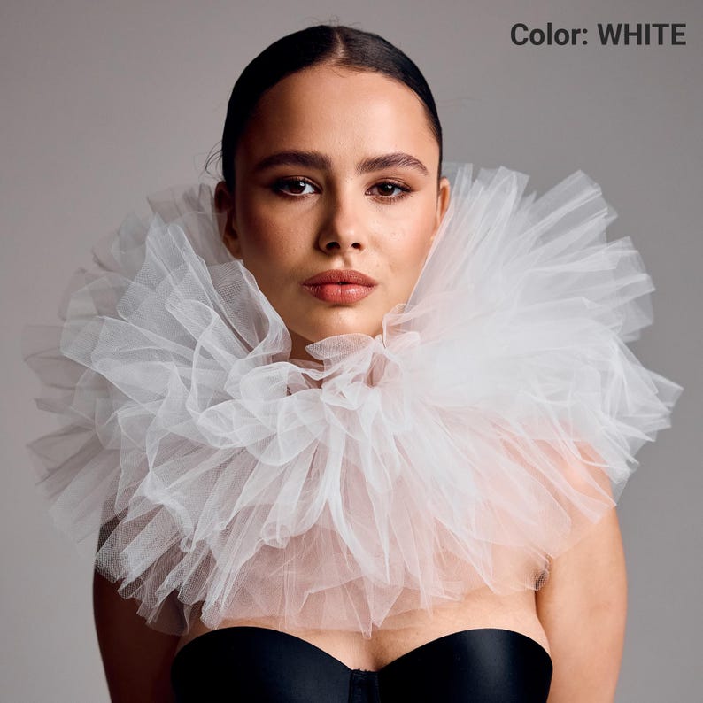 May include: A white tulle collar with multiple layers, creating a voluminous, ruffled effect. The model is wearing a black top. The text "Color: WHITE" is visible in the upper right corner.