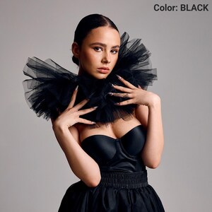 May include: A black strapless dress with a layered tulle collar. The dress has a fitted bodice and a flared skirt. The image includes the text "Color: BLACK".