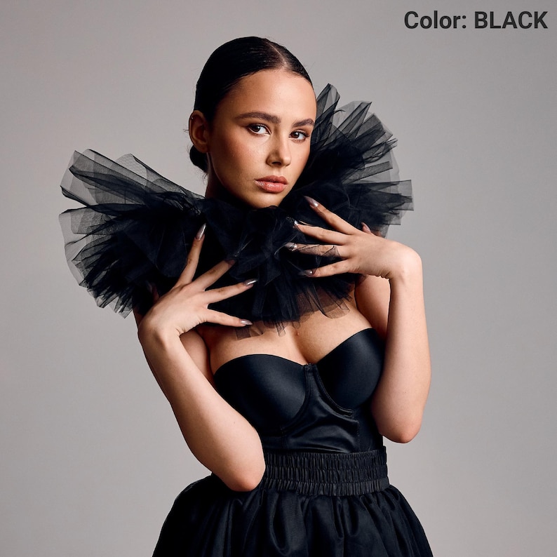 May include: A black strapless dress with a layered tulle collar. The dress has a fitted bodice and a flared skirt. The image includes the text "Color: BLACK".