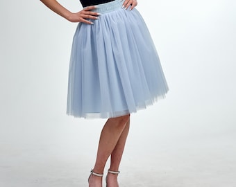 May include: A light blue tulle skirt with a gathered waistband. The skirt is knee-length and has a layered design, creating a full, flowing silhouette. The model is wearing black top and white sandals.