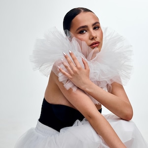 May include: A person wearing a white tulle collar and a black top. The person is also wearing a white tulle skirt. The nails are painted silver.