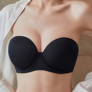 May include: A black strapless bra with a smooth, seamless design. The bra is made of a soft material and has a classic silhouette. A white button-down shirt is partially visible in the background.