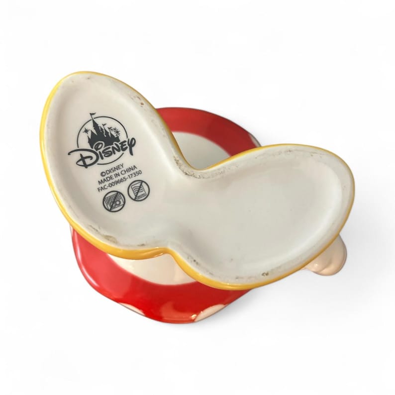 May include: A ceramic Disney mug with a yellow handle and a red and white striped base. The bottom of the mug features the Disney logo and the text "MADE IN CHINA".