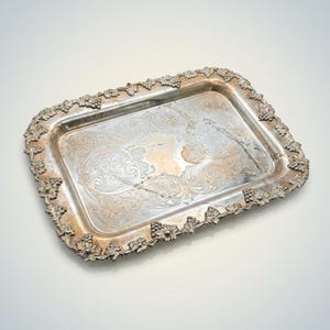 May include: Rectangular silver serving tray with ornate floral and scrollwork detailing. The tray's border is adorned with grape cluster designs. The interior of the tray has a detailed pattern. A vintage piece for serving or display.