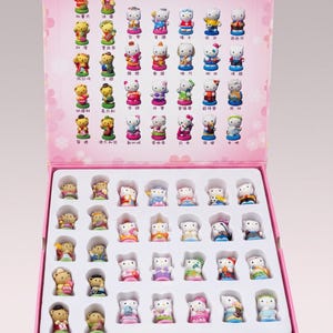 Peut inclure: Un coffret rose contenant de nombreuses figurines Hello Kitty. Les figurines sont vêtues de diverses tenues et poses. La boîte porte le logo Hello Kitty et du texte en plusieurs langues.