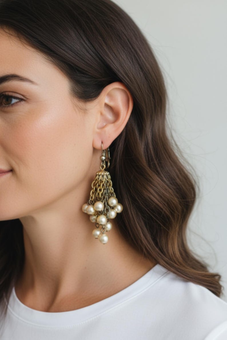 May include: Gold-toned chandelier earrings with a cascade of faux pearls. The earrings feature multiple chains and a cluster of off-white pearls, creating a vintage-inspired look. The earrings are designed with a hook closure.