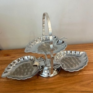May include: A silver-coloured, three-tiered serving tray with leaf-shaped dishes. The tray has a handle for carrying and is made of a shiny metal. The dishes are arranged in a tiered design, ideal for serving appetizers or desserts.