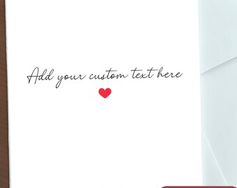 May include: White greeting card with the text "Add your custom text here" in black script, a small red heart, and a "More Font Options" button. The card is on a wooden surface with a white envelope.