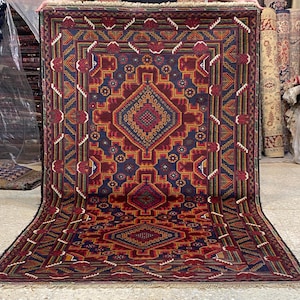 Puede incluir: Una alfombra rectangular grande con un patrón de diamante central en tonos de rojo, azul y dorado. La alfombra presenta intrincados diseños geométricos y un borde con flecos. El diseño general es simétrico, con patrones repetidos.