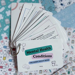 May include: A set of white flashcards bound by a metal ring, titled Mental Health Conditions: The Handy Pocket Book. The cover features a teal label, a light purple label, and small black line drawings of a stethoscope, brain, and pill bottle.