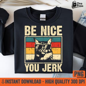 Puede incluir: Sudadera negra con un diseño gráfico de un gato con gafas de sol, sobre un fondo retro de bloques de color. El texto "BE NICE YOU JERK" está encima y debajo de la imagen del gato. El diseño tiene un estilo vintage y humorístico.