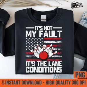 May include: A navy blue sweatshirt featuring a bowling design. The design includes a red bowling ball and pins, set against an American flag background. The text reads "IT'S NOT MY FAULT IT'S THE LANE CONDITIONS."