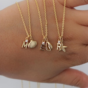 May include: Gold-colored necklaces with initial pendants. Each necklace features a delicate chain and a charm with a letter and a small gemstone. The charms include the letters M, E, and R, along with seashell and starfish designs.