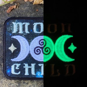 Op de afbeelding: Geborduurde patch met de woorden "MOON CHILD" in lichtblauw, met een maan en ster ontwerp. De patch gloeit groen in het donker en toont de maan en ster. De achtergrond is donkerblauw met een sterrenpatroon.