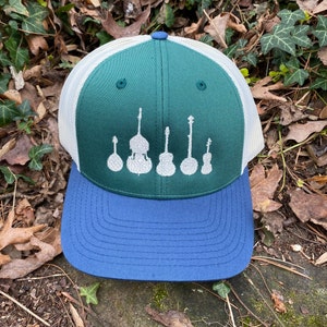 Pode incluir: Bon&eacute; de caminhoneiro verde e azul com costas em malha branca. O painel frontal apresenta um design branco de instrumentos musicais, incluindo um banjo, contrabaixo e guitarras. Estilo cl&aacute;ssico.