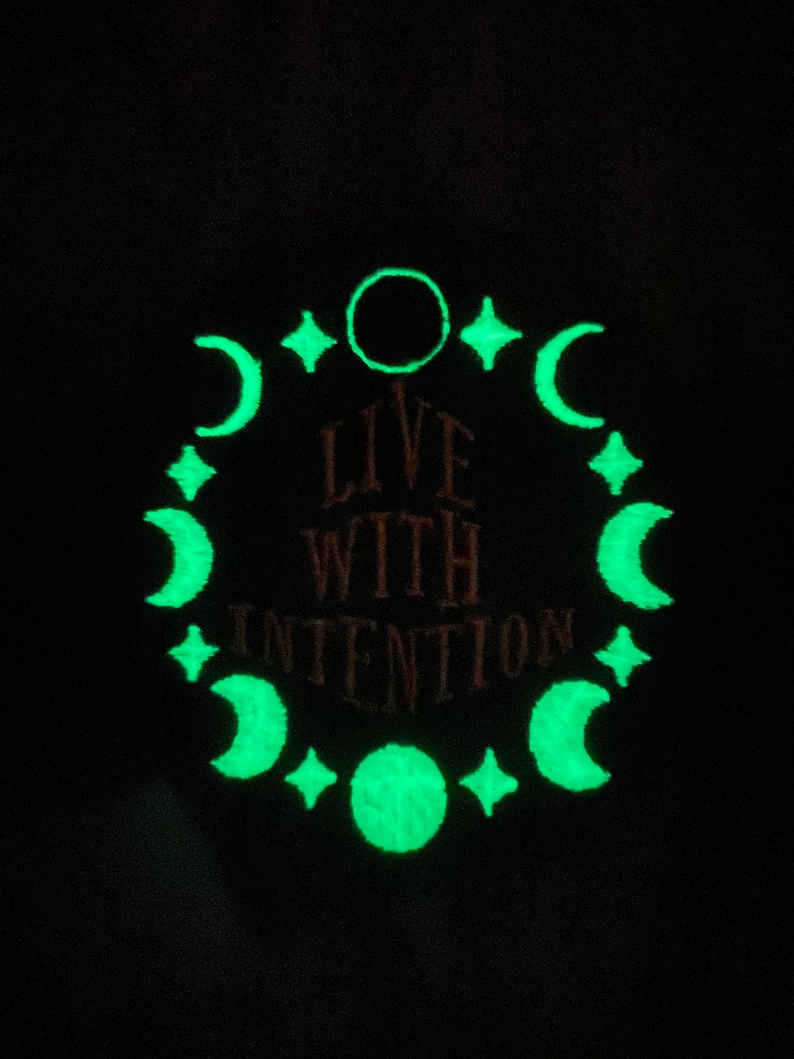 May include: A dark background with a glowing green design. The design includes crescent moons, stars, and a circle, encircling the reddish-brown text "LIVE WITH INTENTION".
