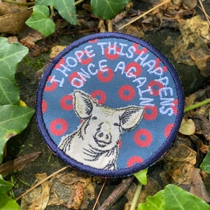 May include: Round patch with a blue background featuring a pig illustration and the text "I HOPE THIS HAPPENS ONCE AGAIN" in white. The pig is white with black details, and the background has red circles.