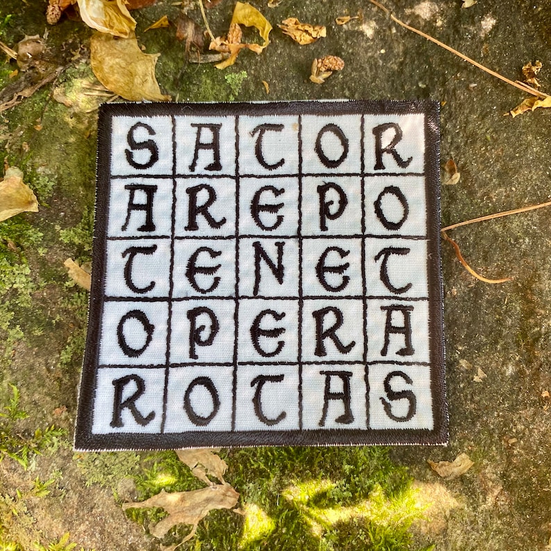 May include: Square patch with the text "SATOR AREPO TENET OPERA ROTAS" in black, block letters. The text is arranged in a grid pattern on a light blue background, with a black border. The patch is likely embroidered or printed.