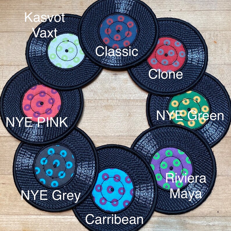 Pu&ograve; includere: Una collezione di otto sottobicchieri circolari neri che assomigliano a dischi in vinile. Ogni sottobicchiere presenta un design centrale unico con vari colori, tra cui blu, rosso, verde e viola, e scritte come "Classic" e "Riviera Maya".