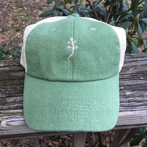 May include: A green baseball cap with a white mesh back and a curved brim. The front of the cap features a white embroidered lizard design. The cap is made of a textured fabric and has a button on top.