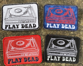 May include: Four rectangular patches featuring a turntable design with the text "PLAY DEAD". The patches are in white, blue, red, and black, with contrasting thread colors for the turntable and text.