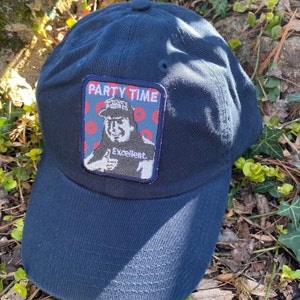 K&ouml;nnte beinhalten: Marineblaue Baseballkappe mit einem Aufn&auml;her mit der Aufschrift "PARTY TIME" &uuml;ber einer Illustration einer Person, die einen Daumen hoch zeigt. Der Aufn&auml;her enth&auml;lt auch das Wort "Excellent".