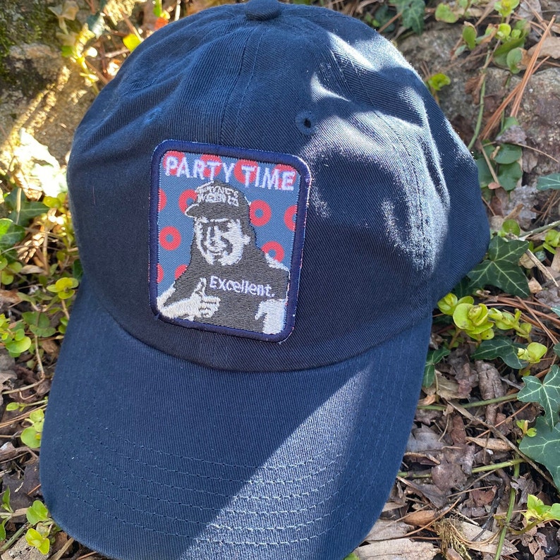 K&ouml;nnte beinhalten: Marineblaue Baseballkappe mit einem Aufn&auml;her mit der Aufschrift "PARTY TIME" &uuml;ber einer Illustration einer Person, die einen Daumen hoch zeigt. Der Aufn&auml;her enth&auml;lt auch das Wort "Excellent".