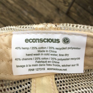 May include: Close-up of a label from an econscious hat. The label is white with black text, listing the materials as 40% hemp, 25% cotton, and 35% recycled polyester. It also includes washing instructions and the brand's website.