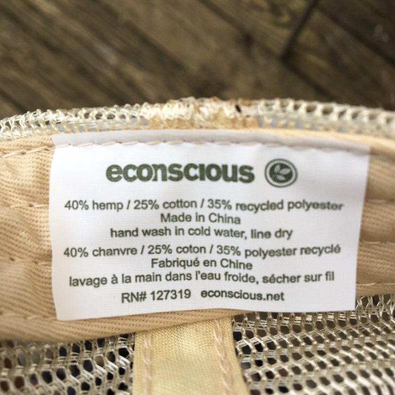 May include: Close-up of a label from an econscious hat. The label is white with black text, listing the materials as 40% hemp, 25% cotton, and 35% recycled polyester. It also includes washing instructions and the brand's website.
