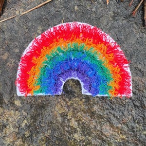 May include: A colorful, handmade rainbow patch with red, orange, yellow, green, blue, and purple yarn. The rainbow is stitched onto a white felt base. The patch is a cheerful, decorative item.