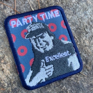 K&ouml;nnte beinhalten: Gestickter Aufn&auml;her mit blauem Rand und blauem Hintergrund mit roten Kreisen. Der Aufn&auml;her zeigt ein Cartoon-Bild eines Mannes, der den Daumen hochh&auml;lt, mit dem Wort "Excellent" darunter. Die Worte "PARTY TIME" stehen oben.
