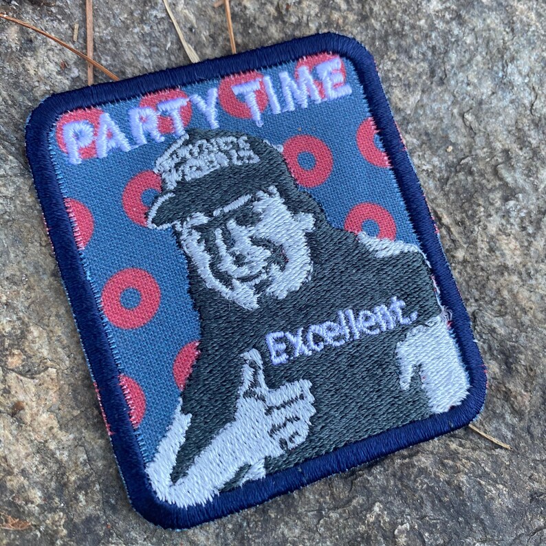 K&ouml;nnte beinhalten: Gestickter Aufn&auml;her mit blauem Rand und blauem Hintergrund mit roten Kreisen. Der Aufn&auml;her zeigt ein Cartoon-Bild eines Mannes, der den Daumen hochh&auml;lt, mit dem Wort "Excellent" darunter. Die Worte "PARTY TIME" stehen oben.