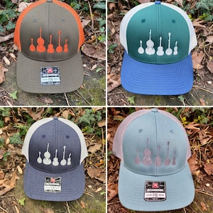 Pode incluir: Quatro bon&eacute;s de caminhoneiro em cores diferentes: verde oliva com malha laranja, verde com malha branca, azul marinho com malha branca e azul claro com malha rosa. Cada bon&eacute; apresenta um design bordado de instrumentos de cordas.