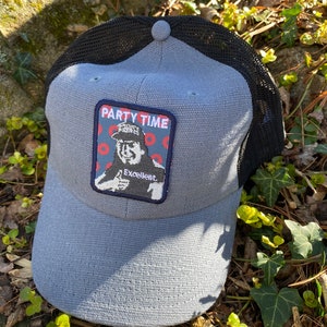 K&ouml;nnte beinhalten: Graue Baseballkappe mit schwarzem Mesh-R&uuml;cken. Die Kappe hat einen Aufn&auml;her mit den Worten "PARTY TIME" und einem Bild eines Mannes, der einen Daumen hochh&auml;lt. Das Wort "Excellent" steht ebenfalls auf dem Aufn&auml;her.