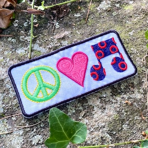 May include: Embroidered patch featuring a peace symbol, a pink heart, and a musical note. The peace symbol is green with a yellow outline. The heart has a textured pattern. The musical note is blue with red circles.