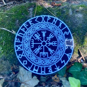 May include: A circular navy blue patch with white embroidered Viking symbols. The design includes a central compass, runes, and Celtic knotwork. The patch is made of fabric and is a dark blue colour with white detailing.