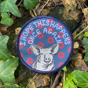 May include: Round patch with a navy blue border and background featuring a pig illustration. The patch has the text "I HOPE THIS HAPPENS ONCE AGAIN" in white. The background has a pattern of red circles.
