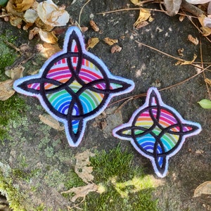May include: Two embroidered patches with a Celtic knot design. The patches feature a rainbow-colored background with a black knot overlay and a white border. The patches are in different sizes.