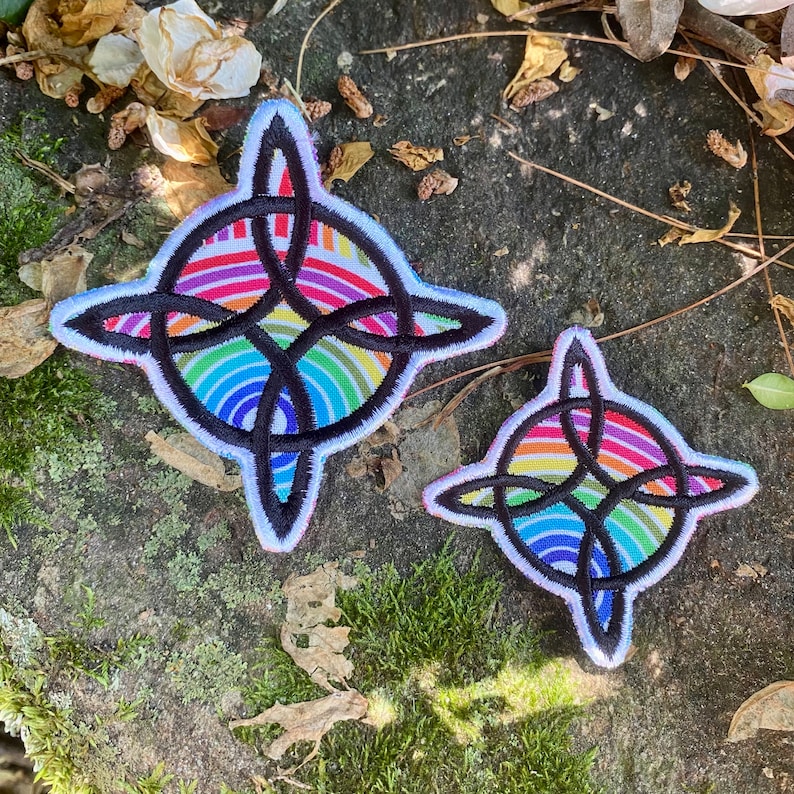 May include: Two embroidered patches with a Celtic knot design. The patches feature a rainbow-colored background with a black knot overlay and a white border. The patches are in different sizes.