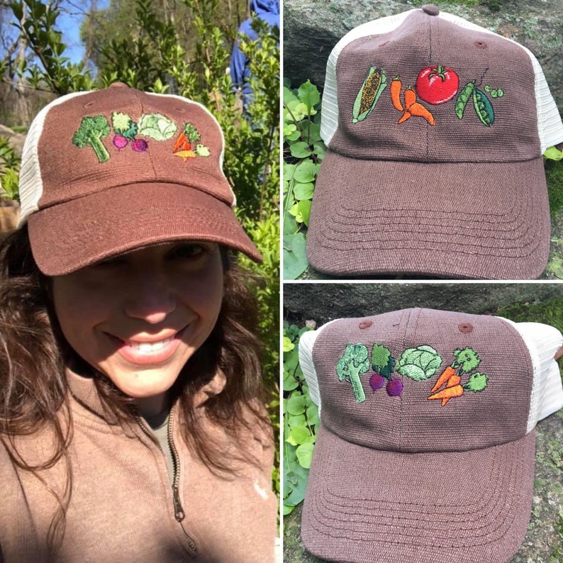 May include: Brown baseball cap with white mesh backing, embroidered with colorful vegetables including broccoli, carrots, and a tomato. The cap has a curved brim and is worn by a person.