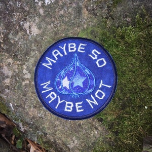May include: A round, blue patch with the words "MAYBE SO MAYBE NOT" in white lettering. The patch features a stylized onion shape with a starry design and a large star in the center.